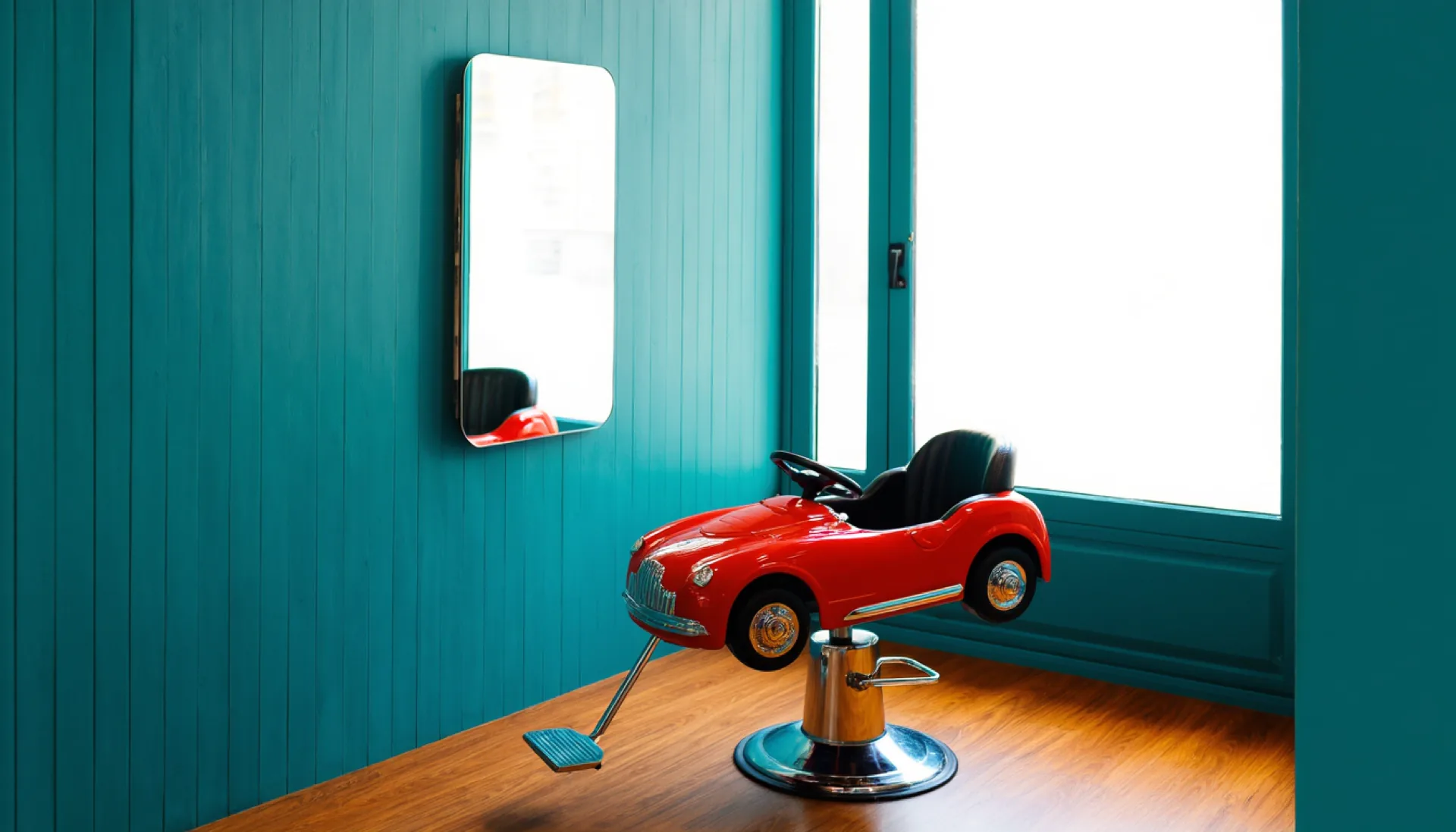 The empty red race-car barber chair in front of the mirror at Papa & Bande, lit by the shop window