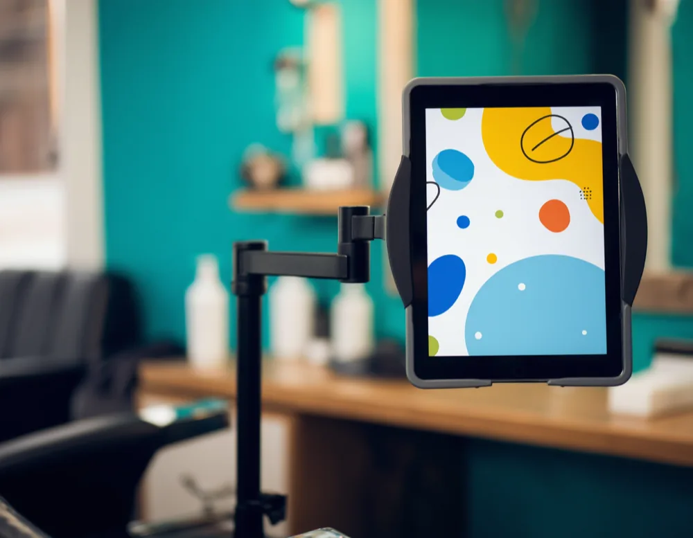 A tablet on an articulated arm beside a barber chair showing colourful animation